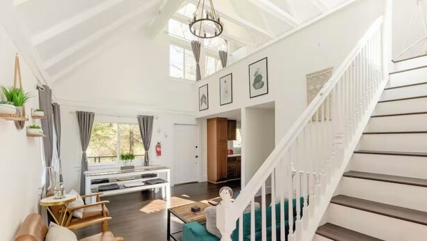 A spacious living area with a high ceiling, a staircase, and a view of the outdoors. - Cozy Treetop A-Frame, Fireplace, Arcade Games, Record Player (Lake Arrowhead)