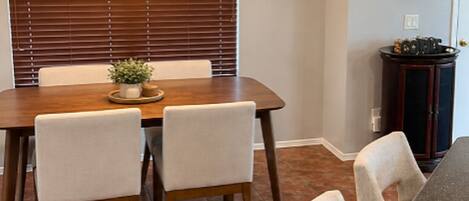 A dining area with a wooden table, four chairs, a hanging light fixture, and a potted plant.