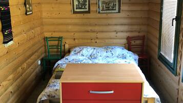 A wooden cabin room with a bed, a red dresser, and framed pictures on the wall.
