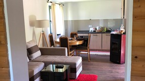 A compact living space with a sofa, a small dining table, and a kitchen area with a refrigerator and stove. - Beautiful wooden house nearby pines forest (Žabljak)