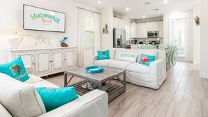 A spacious living room with a white sofa set, teal cushions, and a coffee table. A flat-screen TV is mounted on the wall, and the room has a ceiling fan. - Amazing Margaritaville Holiday Home - Indoor/Outdoor Entertaining Space (Kissimmee)