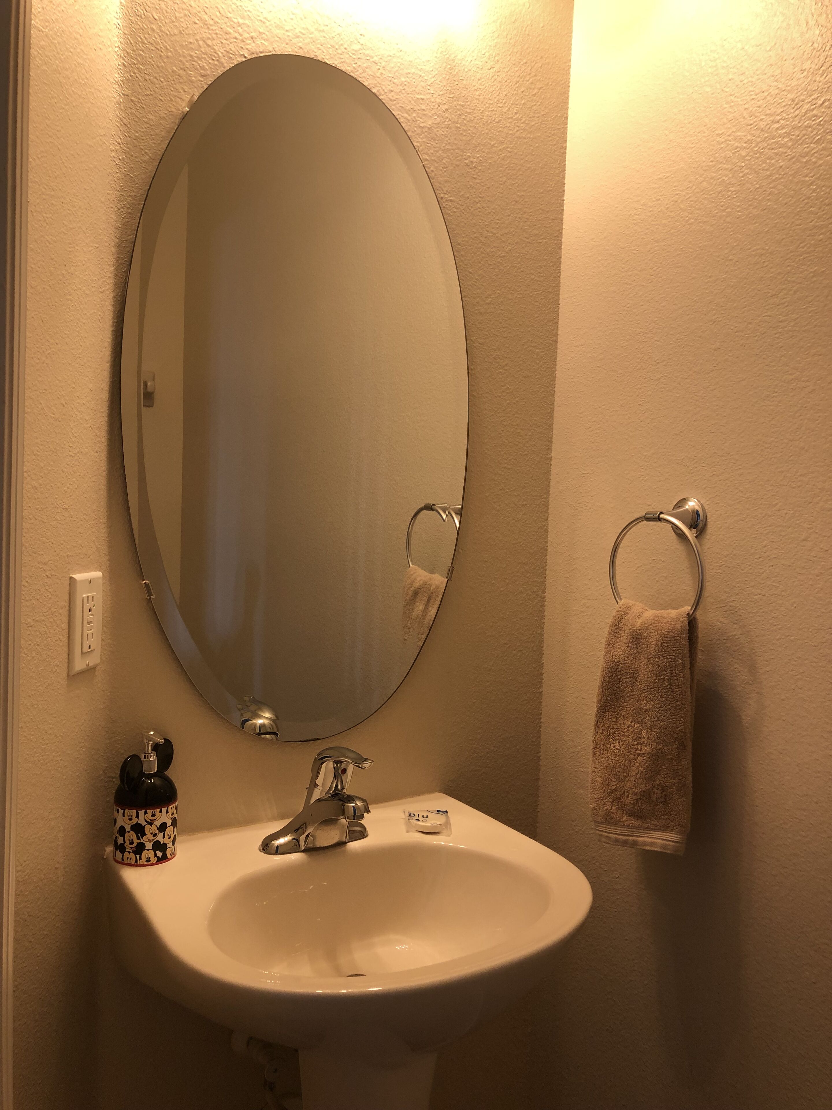 Un bagno con un lavandino bianco, uno specchio rotondo, un portaserviti e un dispenser per sapone.