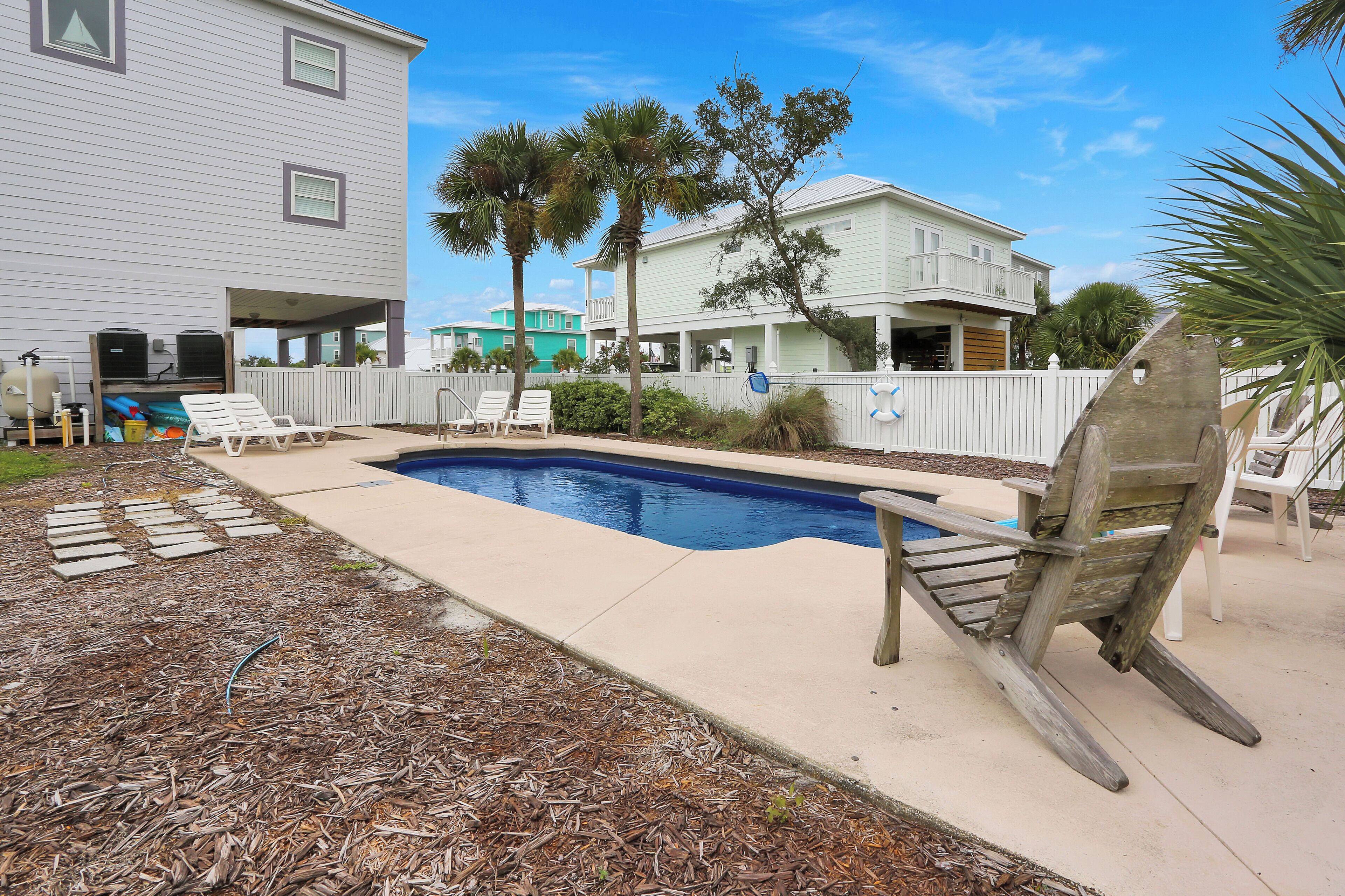 A backyard with a swimming pool, lounge chairs, and a wooden deck.