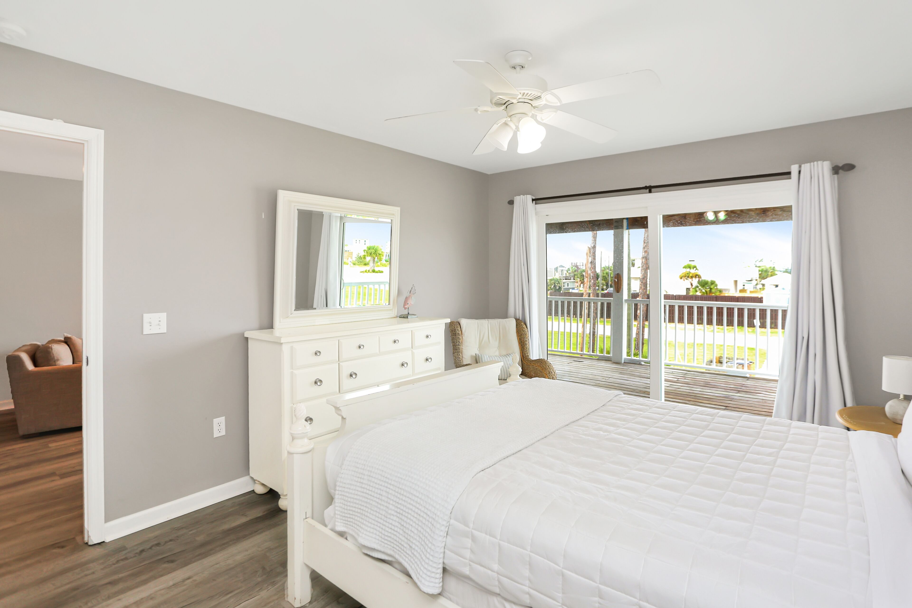 A bedroom with a large bed, a dresser, a ceiling fan, and a sliding glass door leading to a balcony.