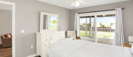 A bedroom with a large bed, a dresser, a ceiling fan, and a sliding glass door leading to a balcony.