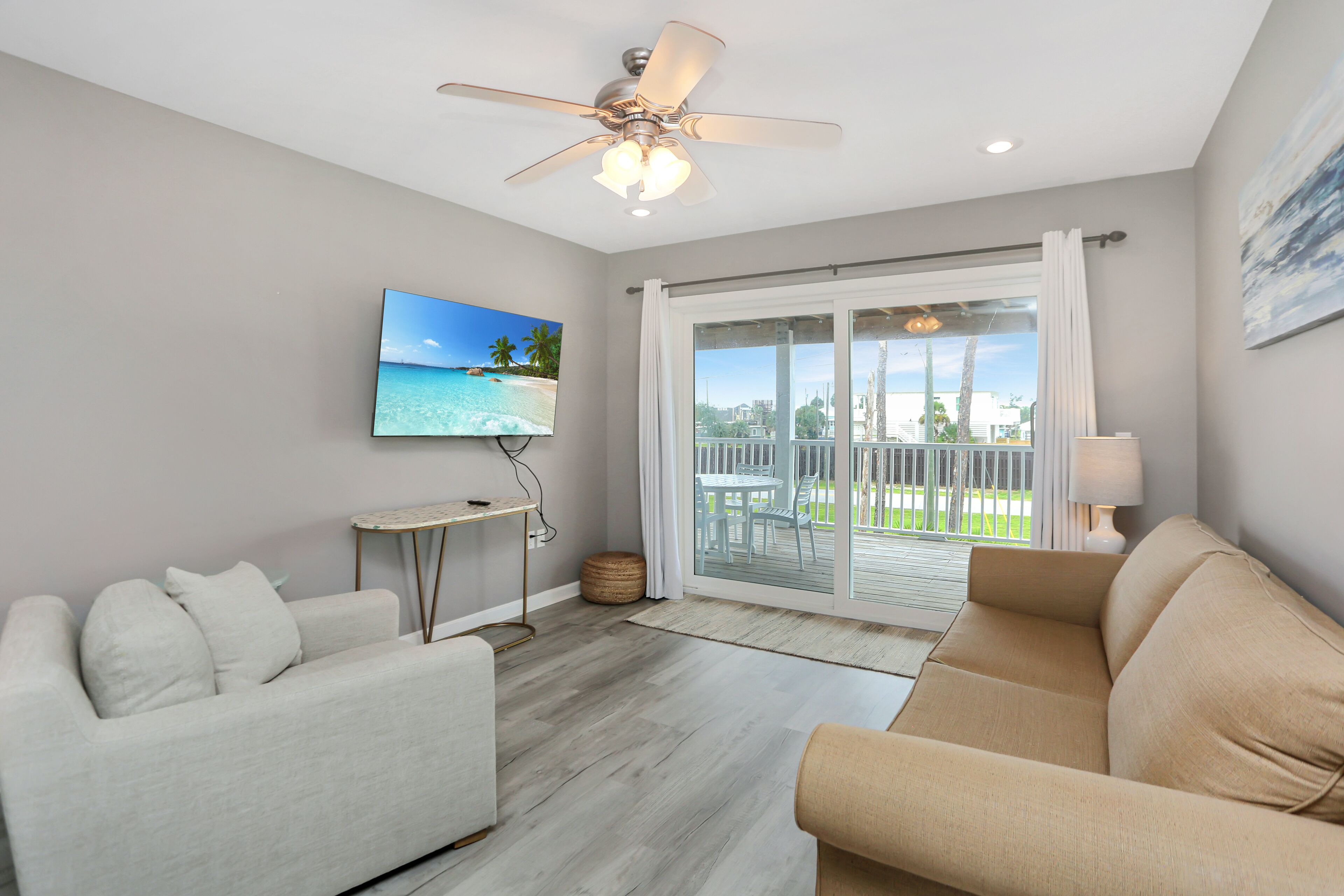 Una sala de estar moderna con ventilador de techo, televisor de pantalla plana, sofá y vista a un balcón con mobiliario exterior.