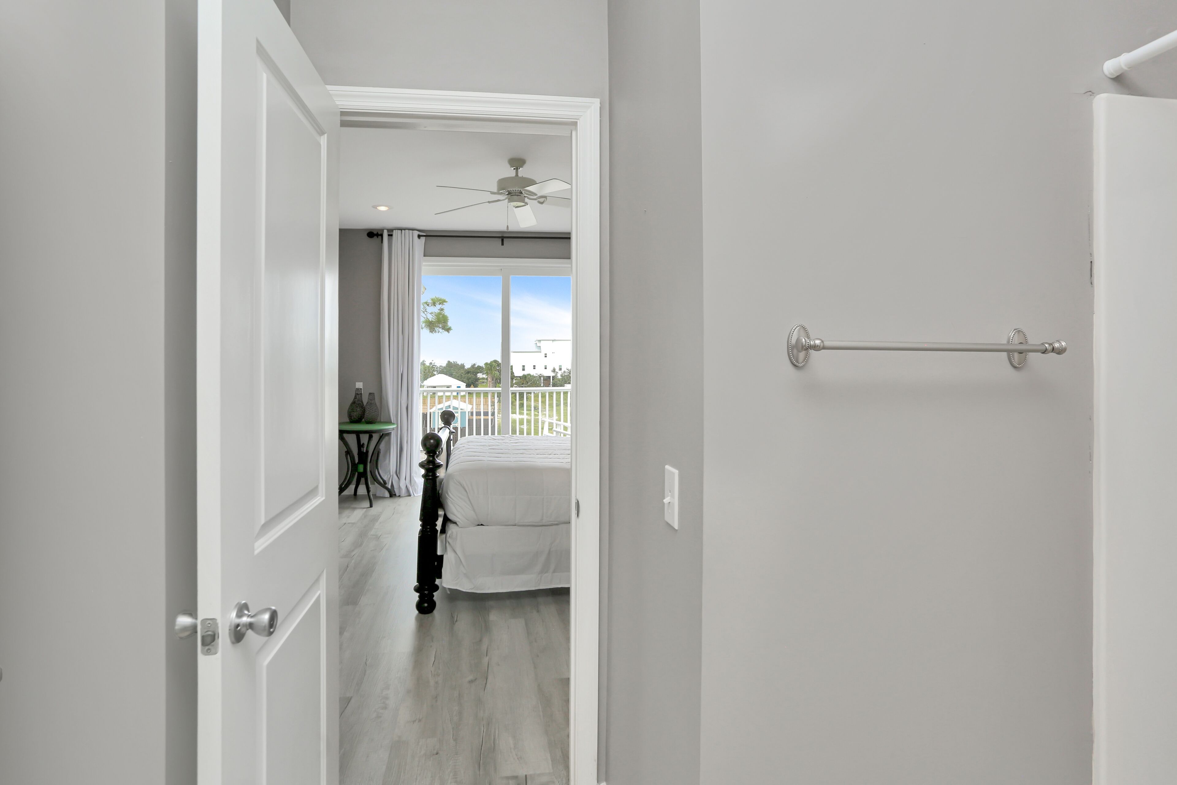 A hallway leading to a bedroom with a bed, a ceiling fan, and a view of the outside.