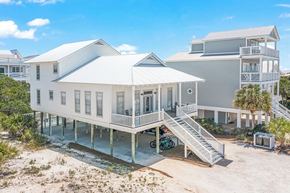 A beachfront house with a balcony, a covered porch, and a staircase leading to the upper level.