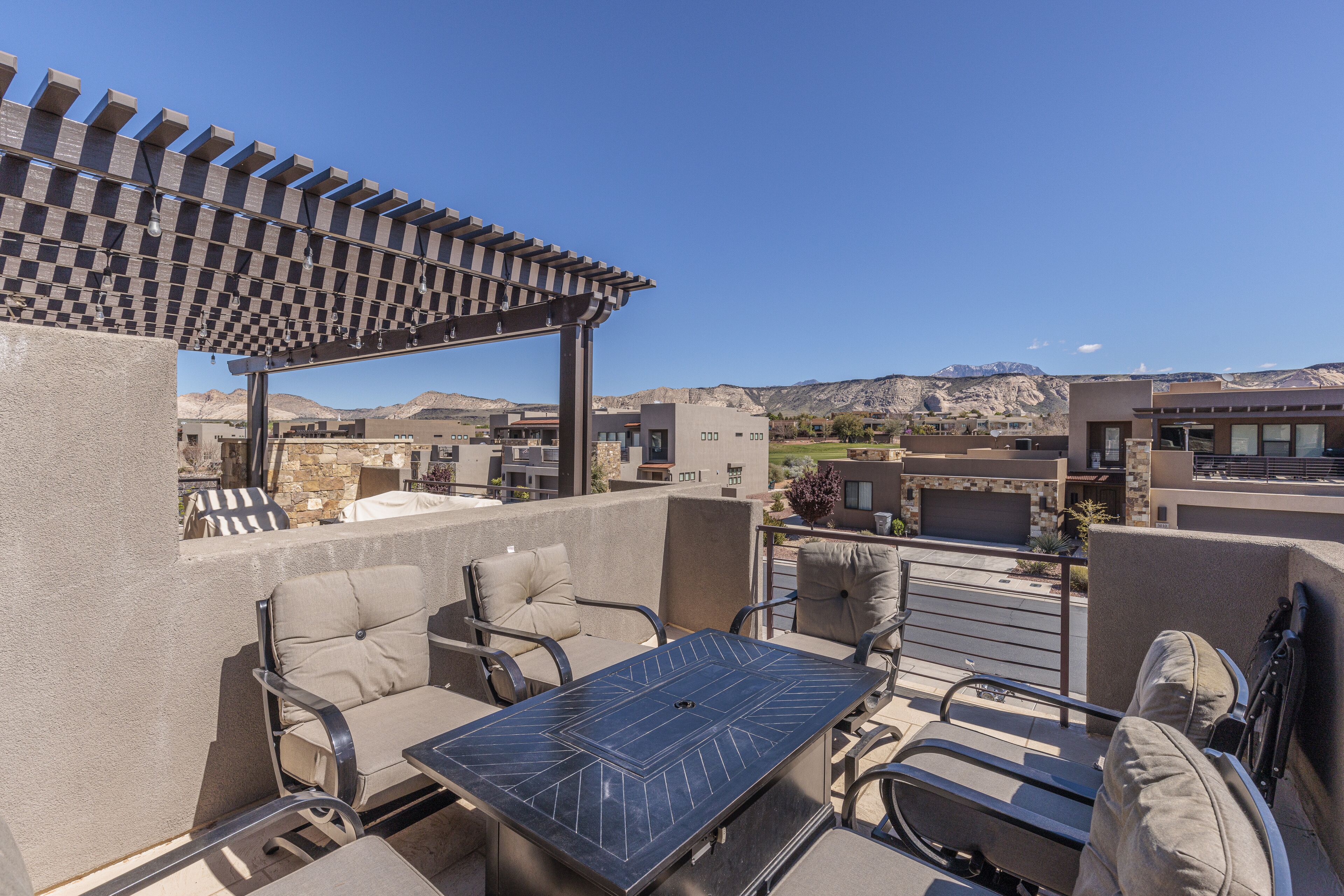 An outdoor patio with a pergola, seating area, and a table.