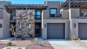 Un immeuble résidentiel moderne à plusieurs étages, doté d’une façade en pierre, d’un patio couvert et d’un garage.