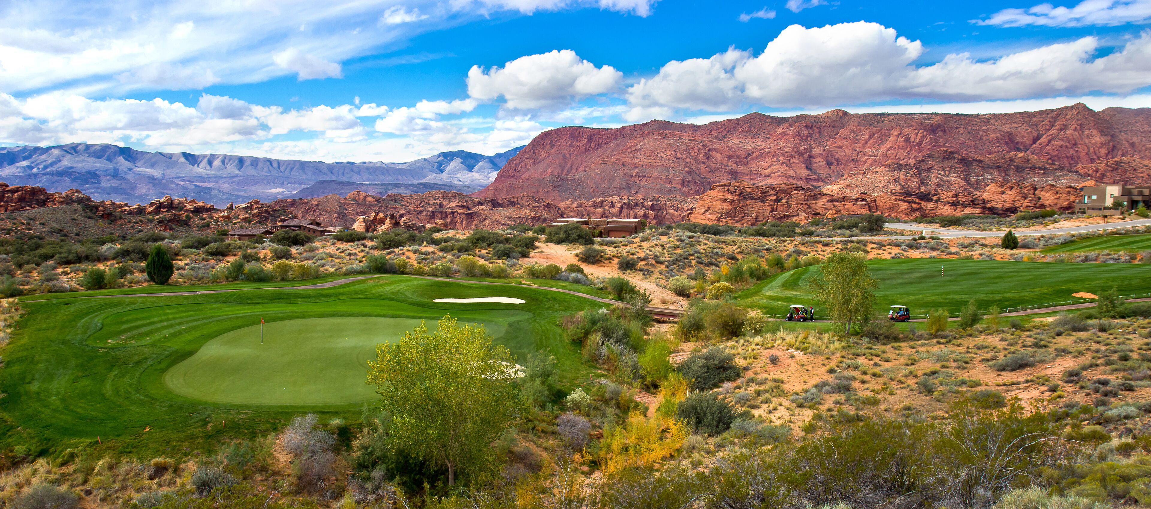 Un parcours de golf situé en plein désert, avec une chaîne de montagnes en toile de fond, un club-house et un ciel dégagé.