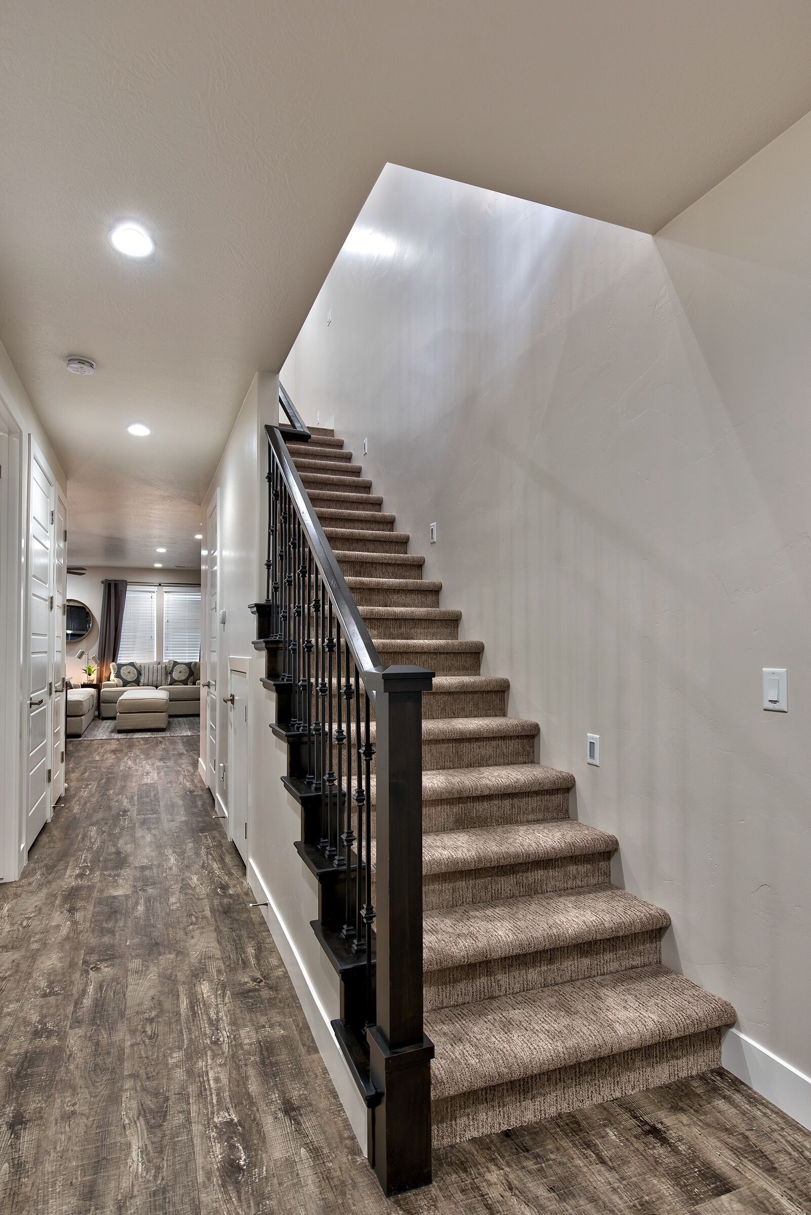 A staircase with a wooden finish and black railing, leading to a landing with a beige carpet.