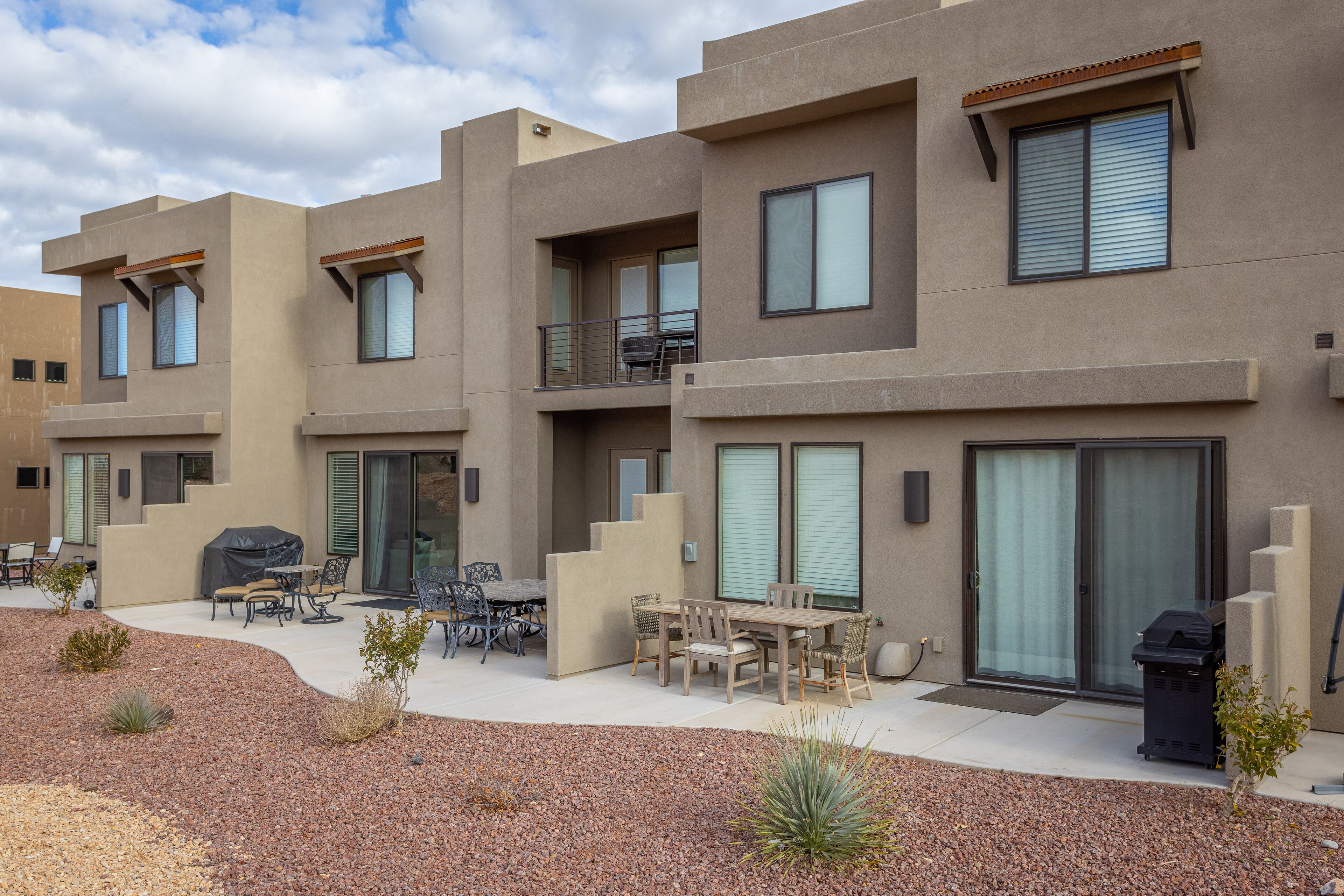 A modern multi-story residential building with a patio area featuring outdoor furniture and a barbecue grill.