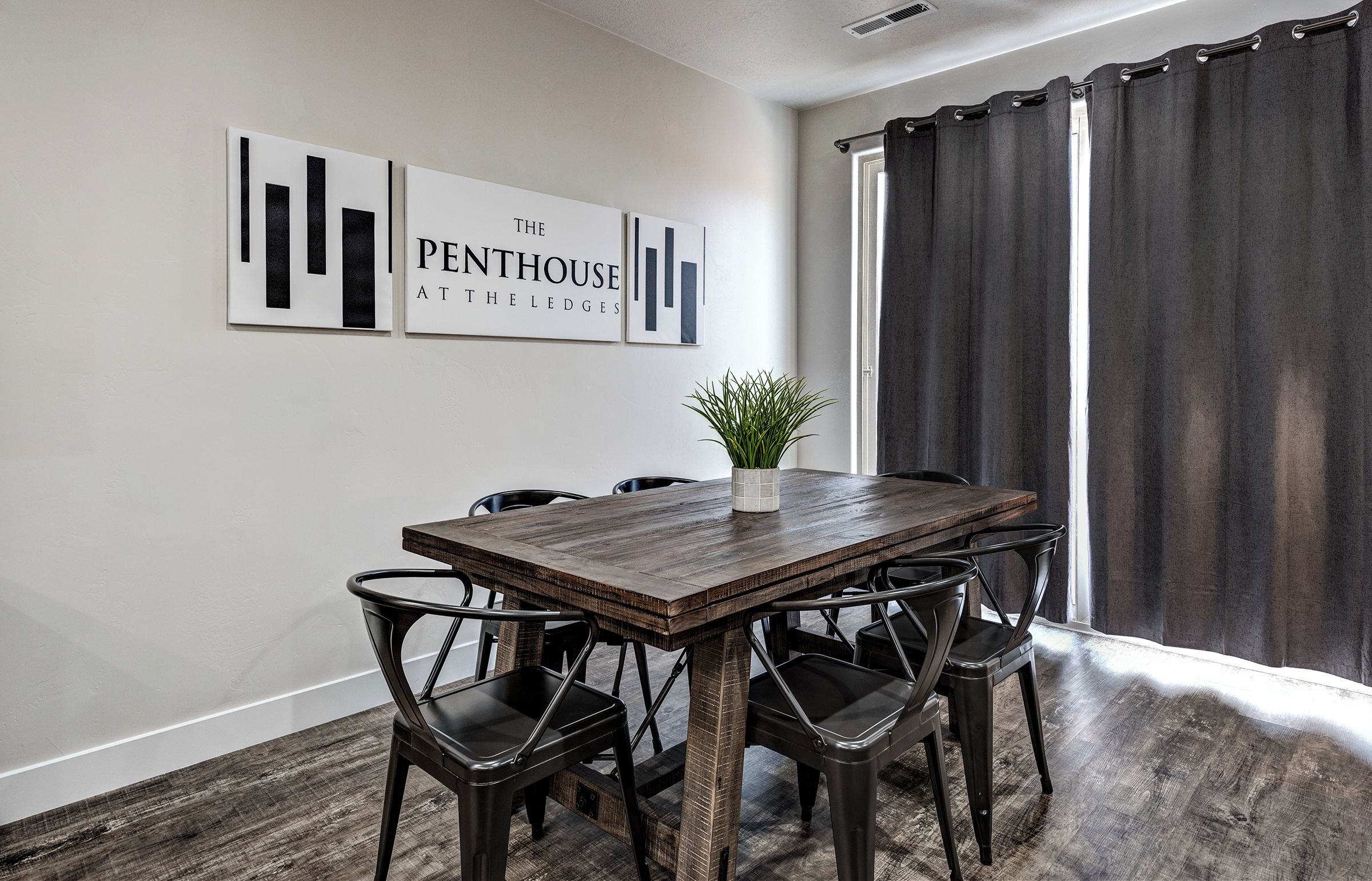 A dining area with a wooden table and black chairs, a potted plant, and two wall-mounted artworks.