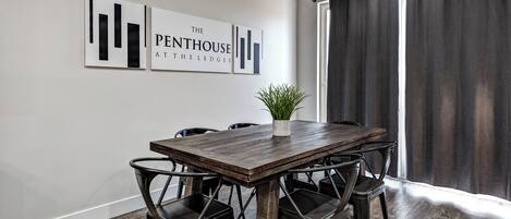 A dining area with a wooden table and black chairs, a potted plant, and two wall-mounted artworks.