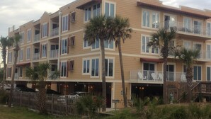 Un hotel de varios pisos con balcones, palmeras y una cerca de madera.