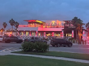 A multi-story building with a restaurant named 'Shaft Life Food Shack' on the ground floor. There are palm trees and a parking lot with cars.