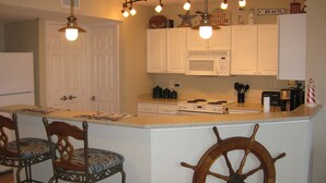 Una cocina con armarios blancos, microondas, estufa y una barra con decoración de timón de barco.