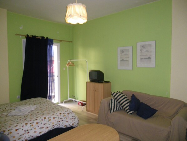 A room with two beds, a sofa, a TV on a cabinet, and two framed pictures on the wall.