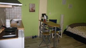 Pieni, käytännöllinen keittiö, jossa on liesi, pesuallas ja pieni pöytä tuoleineen. Huoneessa on myös sänky, jonka päällä on kukkakuviollinen päiväpeite.