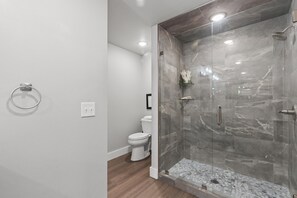 A modern bathroom with a glass-enclosed shower, a toilet, and a ring light on the wall.
