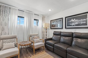 A living room with a brown leather sofa, a wooden side table, a beige armchair, and a patterned rug.
