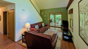 A living room with a brown leather sofa, a lamp, a television, and a large framed map on the wall. - Island Fox Nestled in the Woods on Madeline Island (La Pointe)
