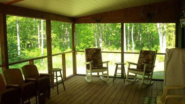 A covered porch with wooden flooring, several chairs, and a table. - Island Fox Nestled in the Woods on Madeline Island (La Pointe)