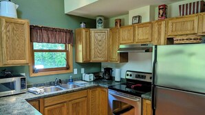 A kitchen with wooden cabinets, a stainless steel refrigerator, a microwave, and a stove. - Island Fox Nestled in the Woods on Madeline Island (La Pointe)