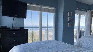 A bedroom with a bed, a dresser, a television, and a balcony with a view of the beach. - Beachfront 2-bedroom condo with breathtaking ocean views from every room! (Fernandina Beach)