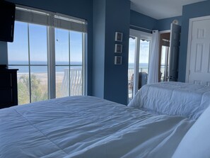 A bedroom with a large bed, a TV, and a view of the beach and ocean through the window. - Beachfront 2-bedroom condo with breathtaking ocean views from every room! (Fernandina Beach)