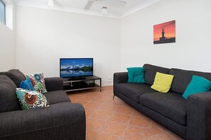 Ein Wohnzimmer mit zwei Sofas, einem Flachbildfernseher und einem Gemälde an der Wand.