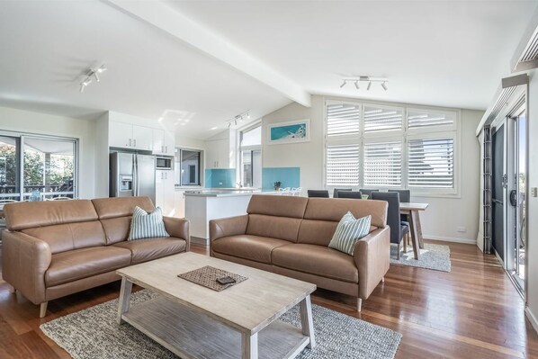 A modern living room with two brown leather sofas, a wooden coffee table, and a kitchen in the background. - Spoil yourself at Seascape (Lennox Head)