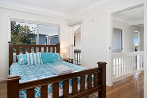 A bedroom with a wooden bed, a view of the outdoors, and a white railing.