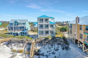 A beachfront property with multiple buildings, including a large house with a blue roof and a smaller structure with a balcony. - Private Pool, Beachfront, Elevator ~ Cape Destiny (Cape San Blas)