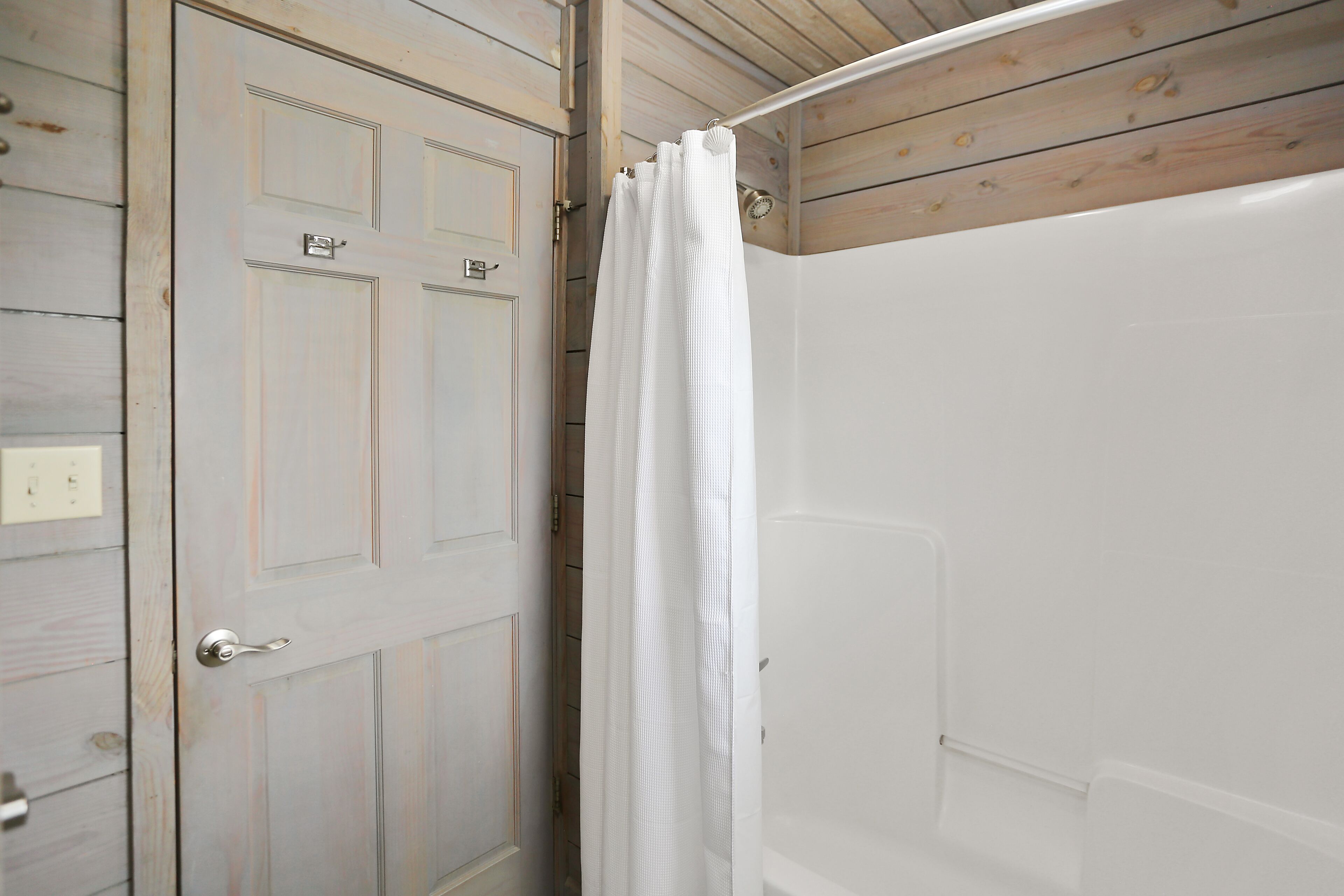 A bathroom with a white shower, a wooden door, and a white curtain.