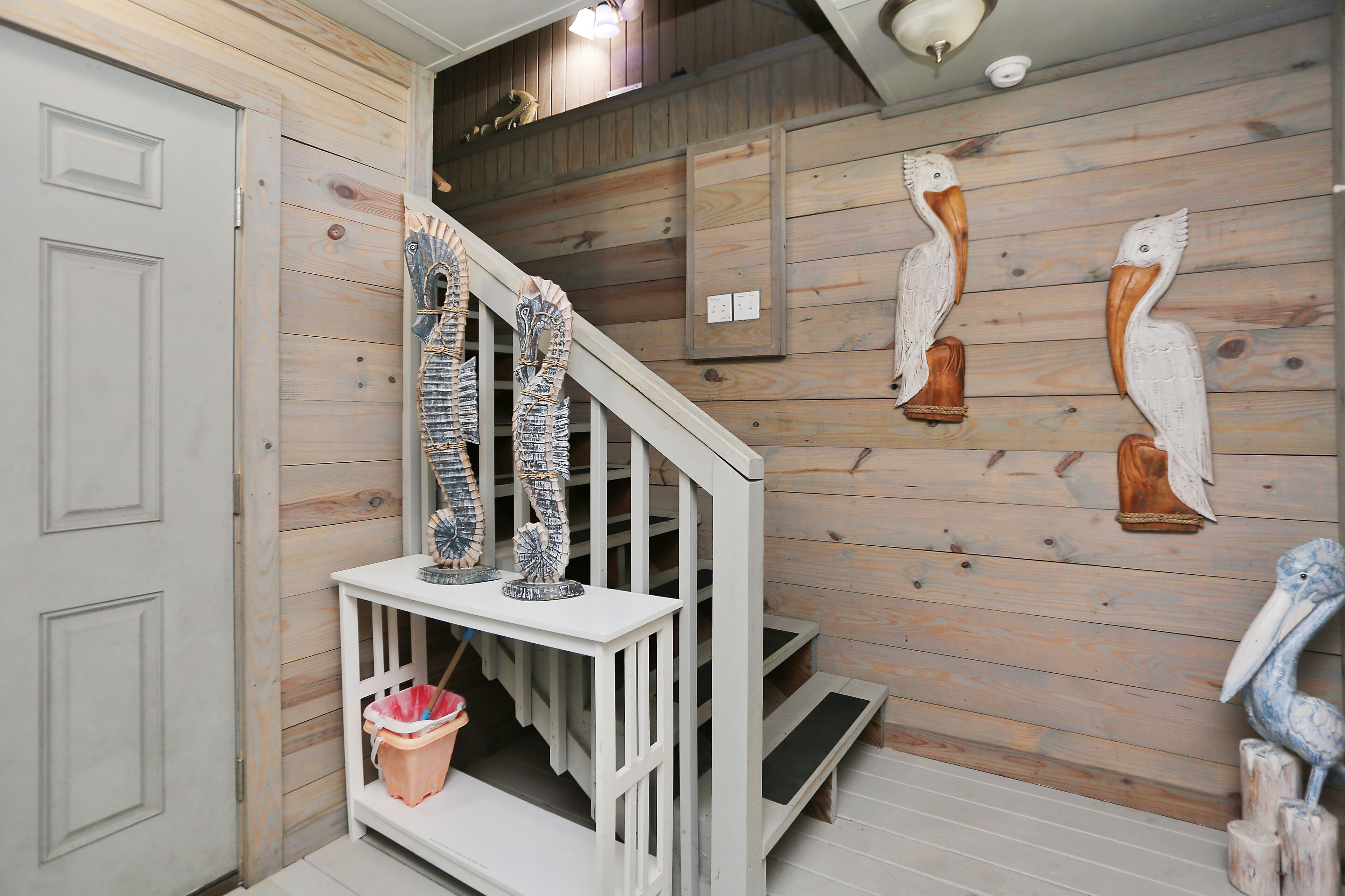 Un escalier en bois avec une rampe blanche, une petite table ornée d’objets décoratifs et des sculptures fixées au mur.