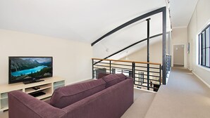 Una sala de estar moderna con un sofá morado, un televisor de pantalla plana sobre un mueble bajo y una escalera con barandilla negra.