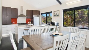 Una cocina moderna con armarios blancos, una isla central y un comedor con sillas blancas.
