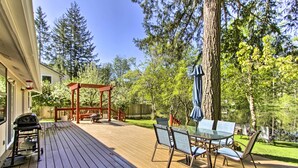 Eine Holzterrasse mit einem Glastisch, Stühlen, einem Grill und einer Schaukel.