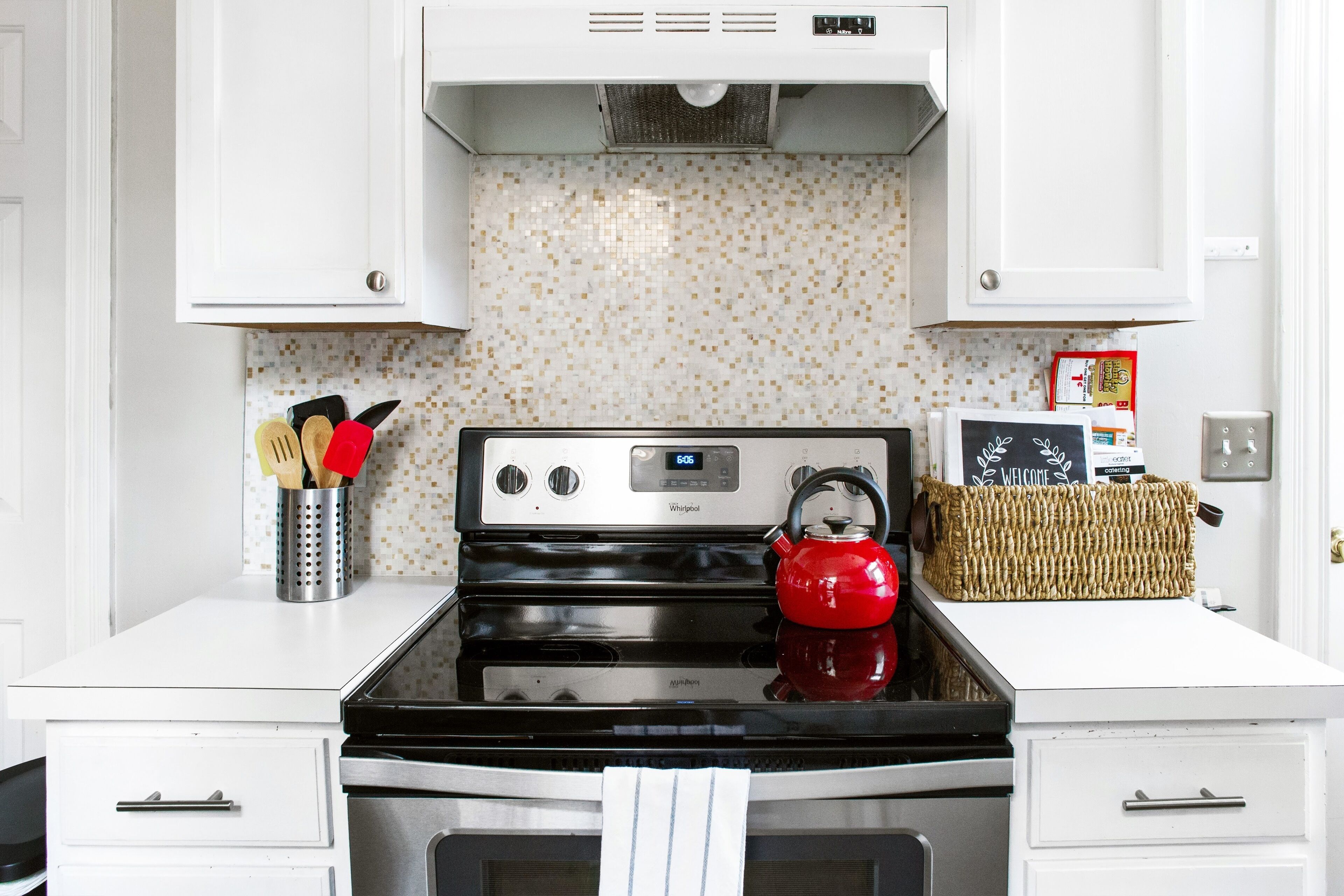 Keittiössä on valkoiset kaapit, ruostumattomasta teräksestä valmistettu liesi ja punainen vedenkeitin.