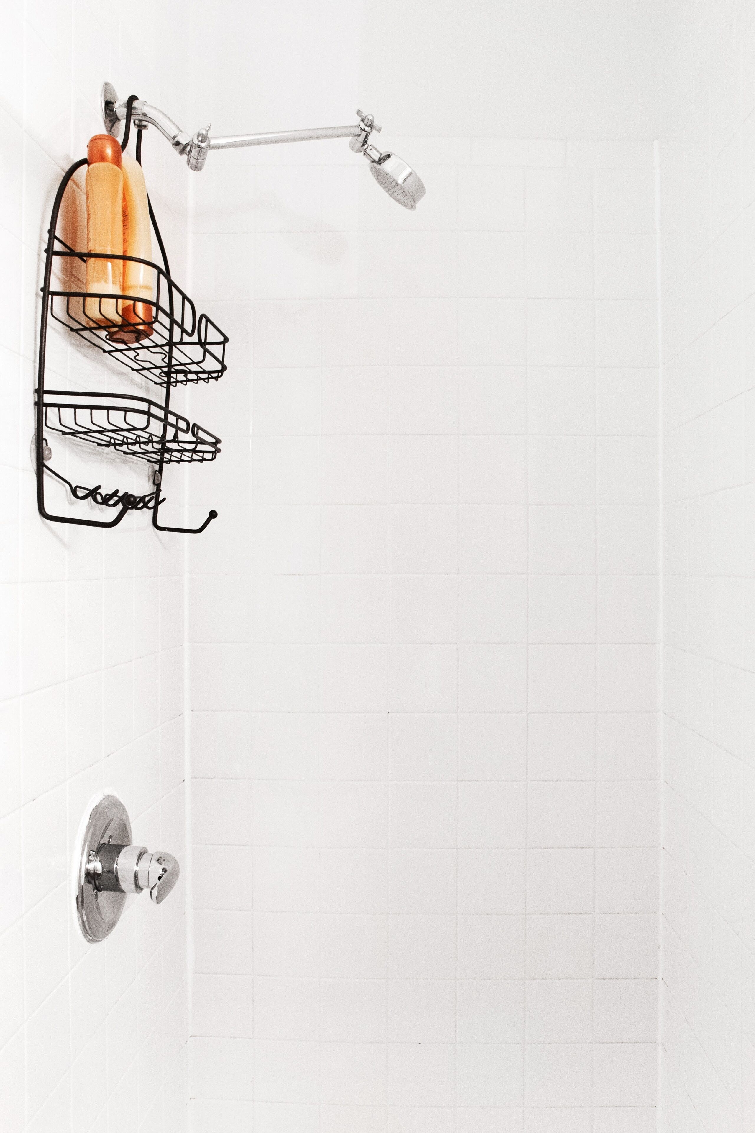 Ein Badezimmer mit weiß gefliester Wand, einem schwarzen Drahtkorb mit Toilettenartikeln und einer Duschbrause.