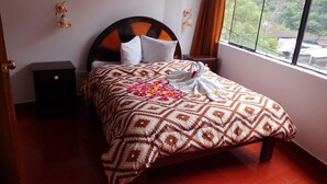 Uma cama bem arrumada com colcha estampada, toalha decorativa e pétalas de rosa sobre a cama.