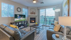 A modern living room with a fireplace, leather sofas, a flat-screen TV, and a balcony with a view. - Superstition Lakes Condo, A+ Golf View, Comm Htd POOL & SPA; Walk to Mall & Theater (Mesa)