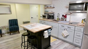 Eine kompakte Küche mit Mikrowelle, Toaster und Spüle. Ein kleiner Barhocker und ein Stuhl sind vorhanden.