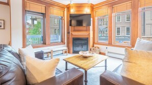 A cozy living room with a fireplace, wooden paneling, a television, and large windows. - Heart of the Center Village!  Walk to everything! Free WiFi & Parking (Copper Mountain)
