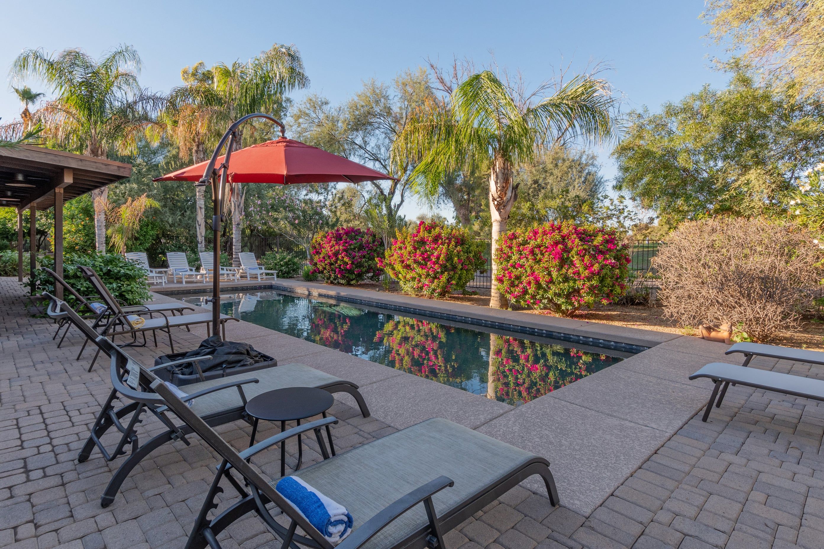 A pool area with lounge chairs, a covered seating area, and a red umbrella.