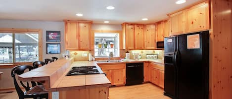 A modern kitchen with wooden cabinets, a black refrigerator, and a central island with a stove.