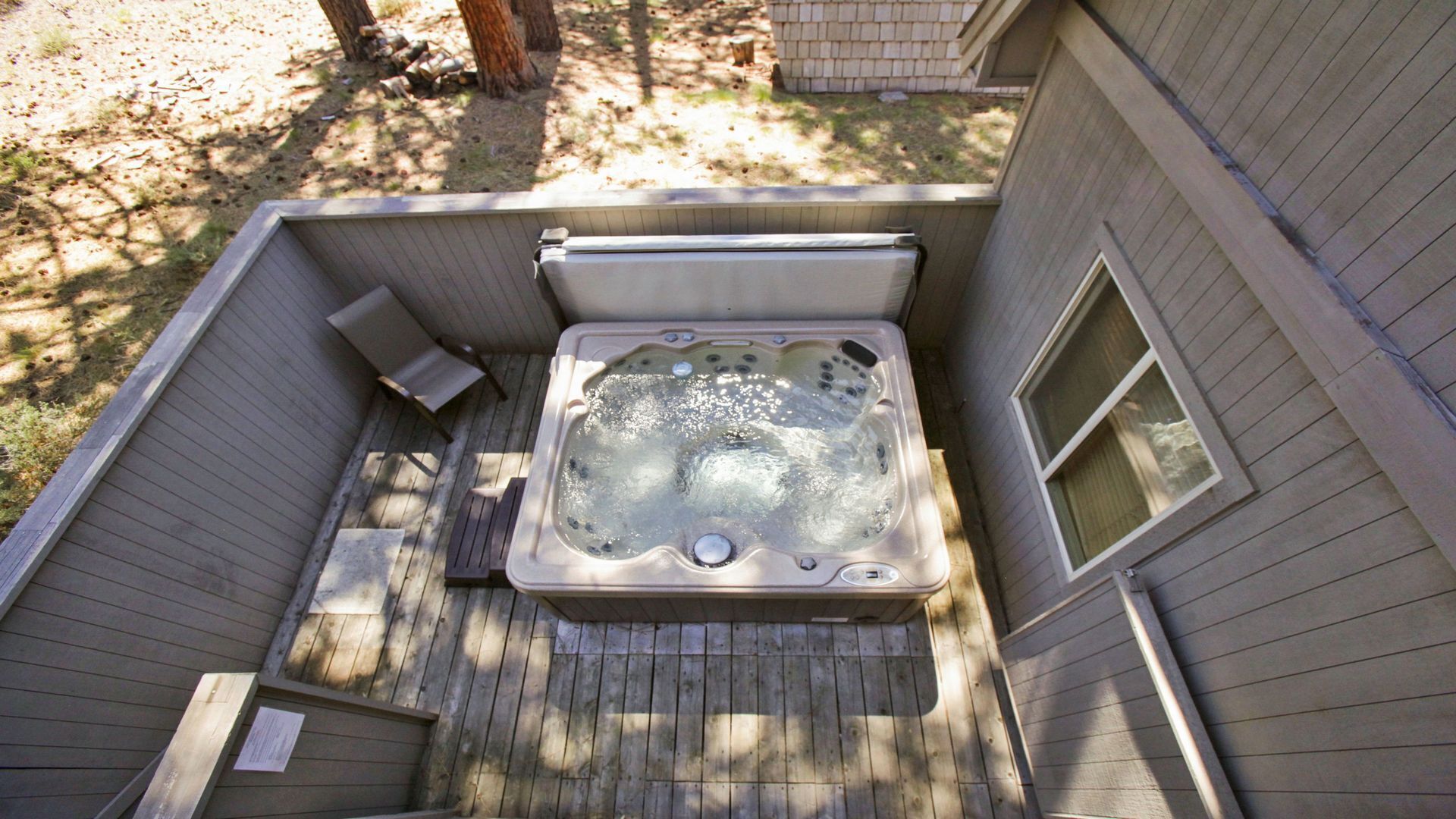 A hot tub on a wooden deck with a window on the side.
