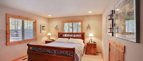 A bedroom with a wooden bed, two bedside tables with lamps, a large window, and a framed picture on the wall.